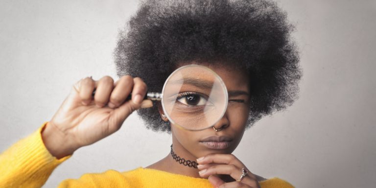 Young,Woman,Looks,Through,A,Magnifying,Glass